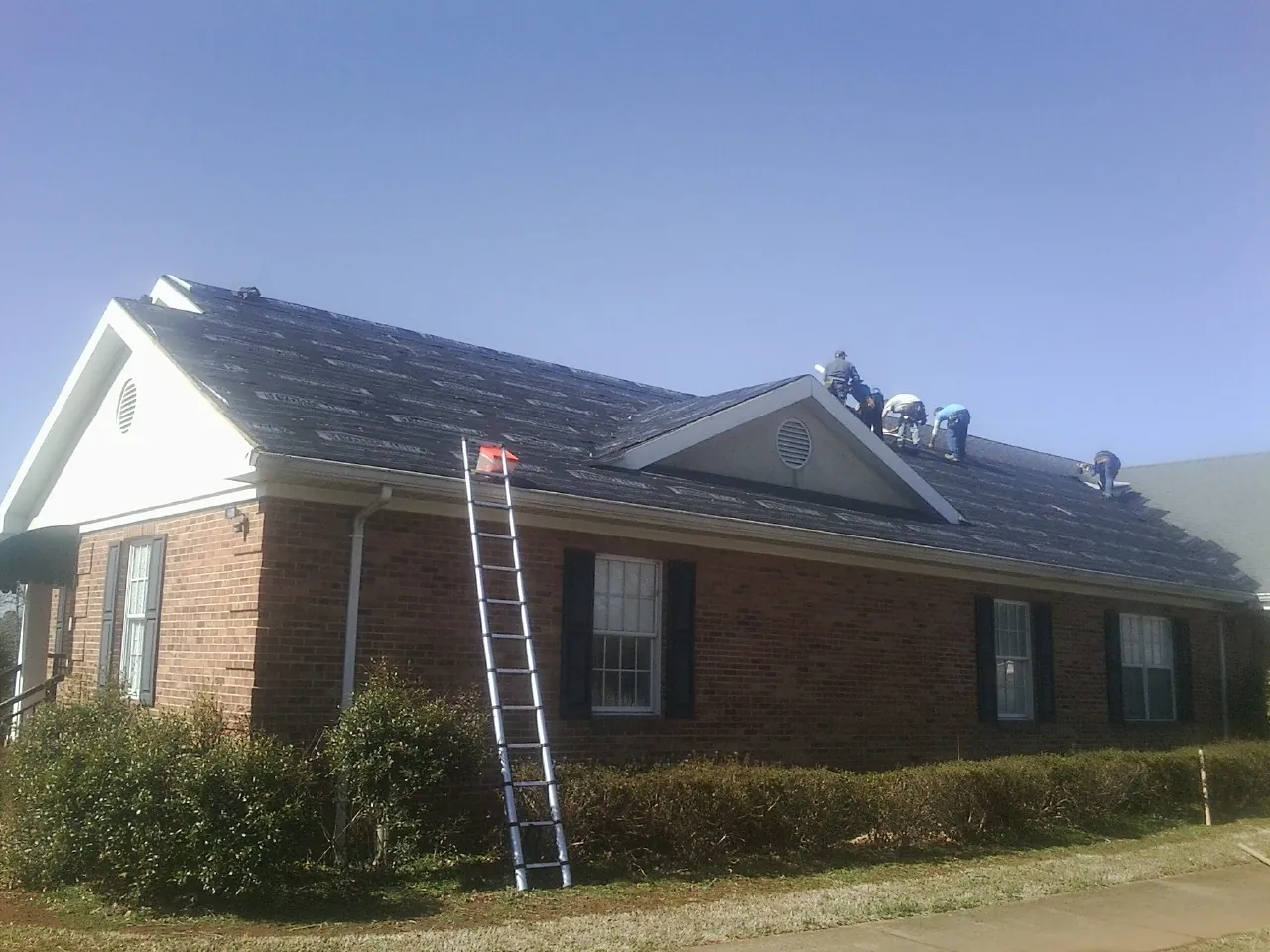 Crew tearing shingles off a brick ranch roof with a ladder set — Metal Roof Repair work by our crew in Bicknell