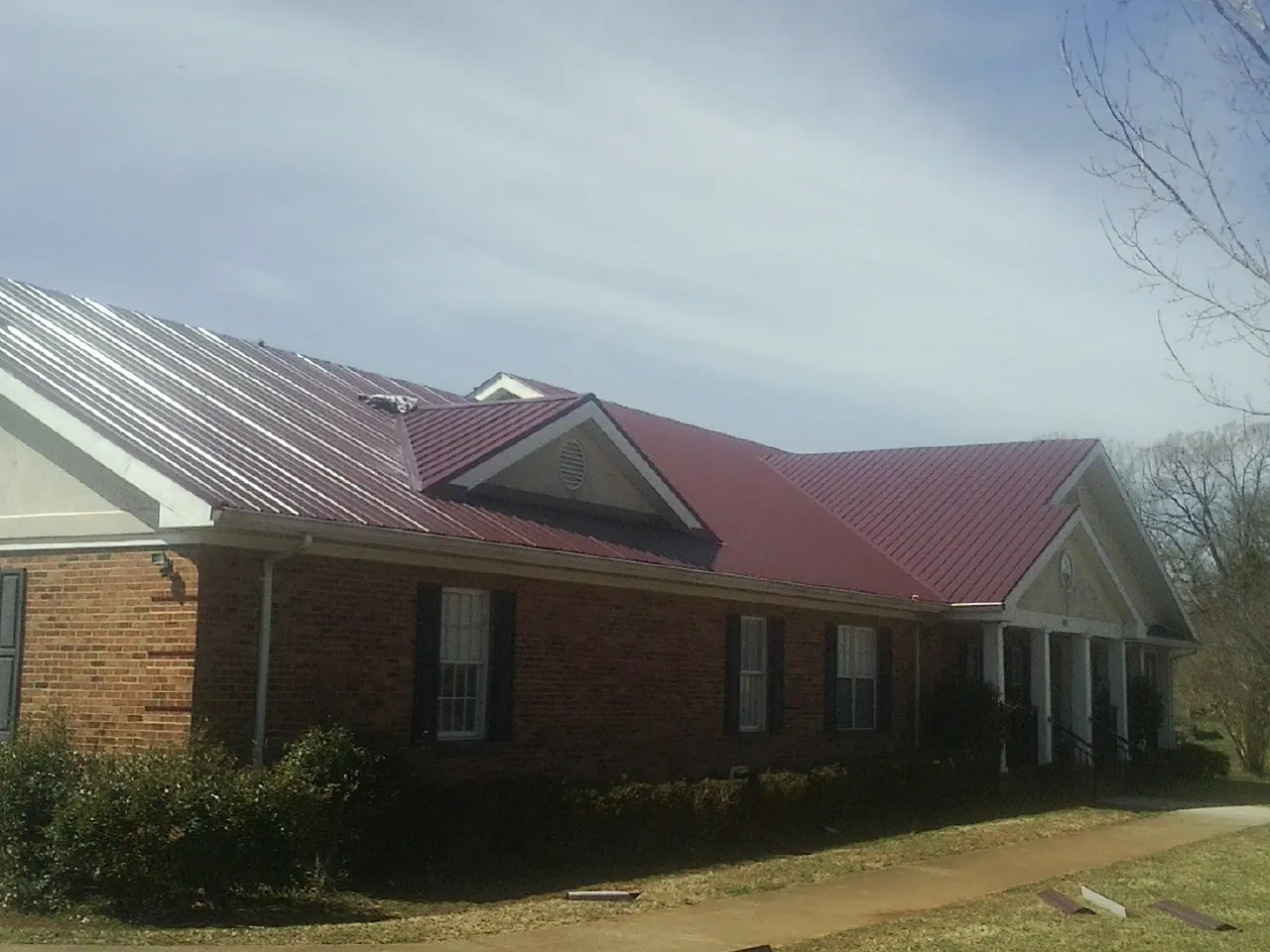 Red metal roof with gabled entries on a long brick building, from a Hail Damage Roof Repair job in Bicknell