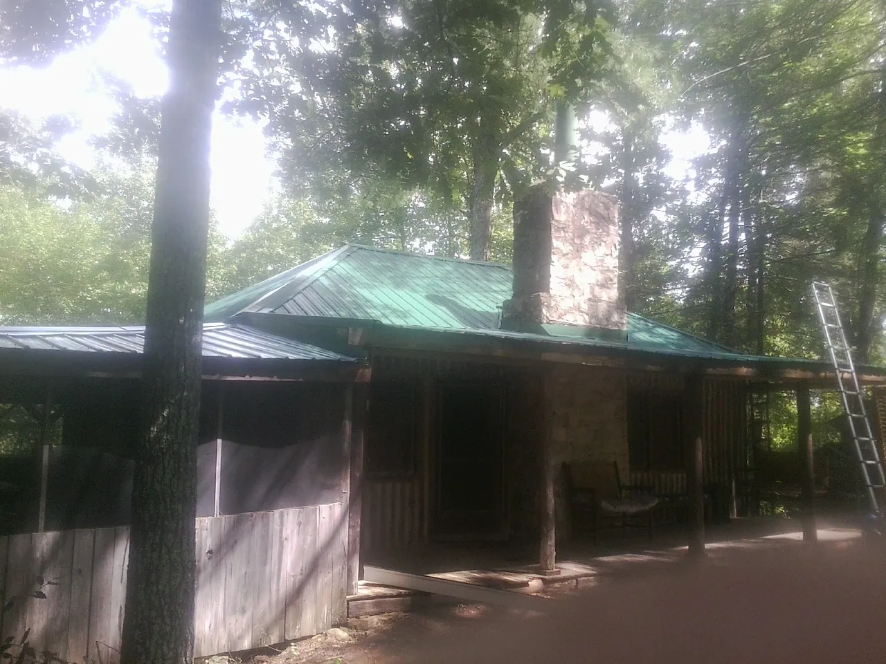 Green metal roof and stone chimney above a log cabin porch in Bicknell