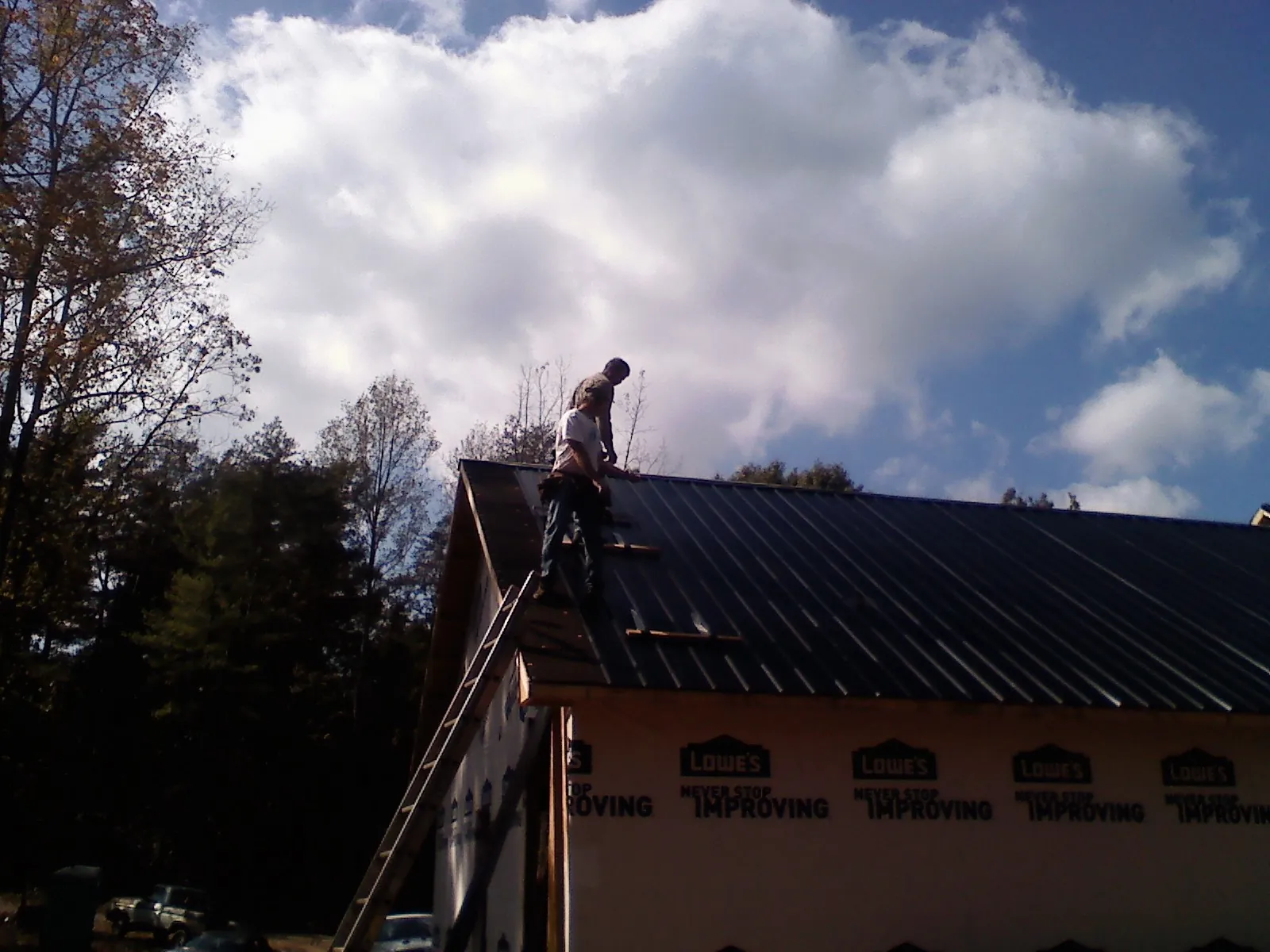 Roofer fastening dark metal panels high against a cloudy sky, from a Roof Inspection job in Bicknell